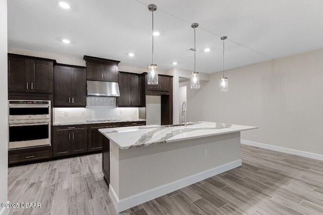 kitchen with hanging light fixtures, tasteful backsplash, a center island with sink, and stainless steel double oven