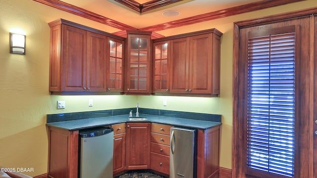 kitchen with dark stone countertops, fridge, crown molding, and sink