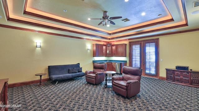 living room featuring ceiling fan, dark carpet, a raised ceiling, and ornamental molding