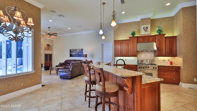 kitchen featuring ornamental molding, ceiling fan with notable chandelier, high end stove, decorative light fixtures, and an island with sink