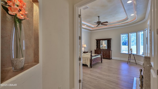 bedroom with a tray ceiling, crown molding, and light hardwood / wood-style flooring