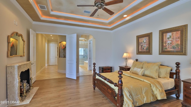 bedroom featuring ensuite bath, ornamental molding, a raised ceiling, ceiling fan, and hardwood / wood-style flooring