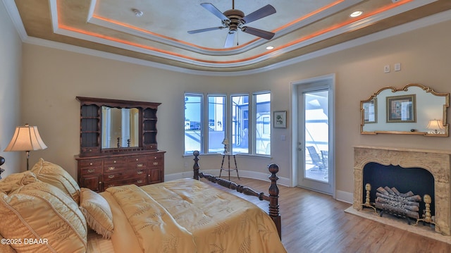 bedroom with ceiling fan, a raised ceiling, light hardwood / wood-style floors, access to outside, and ornamental molding