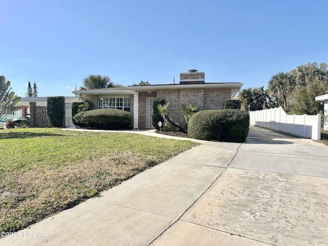 view of front of home with a front yard, fence, brick siding, and a chimney