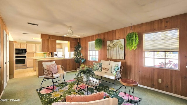 living area featuring visible vents, light carpet, wooden walls, and ceiling fan