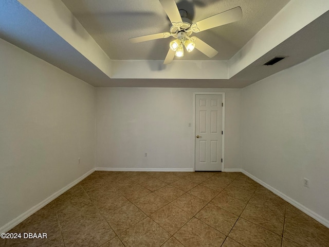 tiled spare room featuring ceiling fan and a tray ceiling