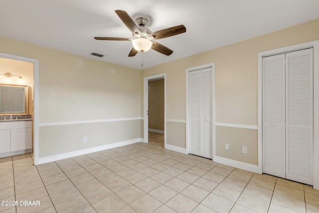 unfurnished bedroom featuring light tile patterned flooring, ceiling fan, sink, and two closets