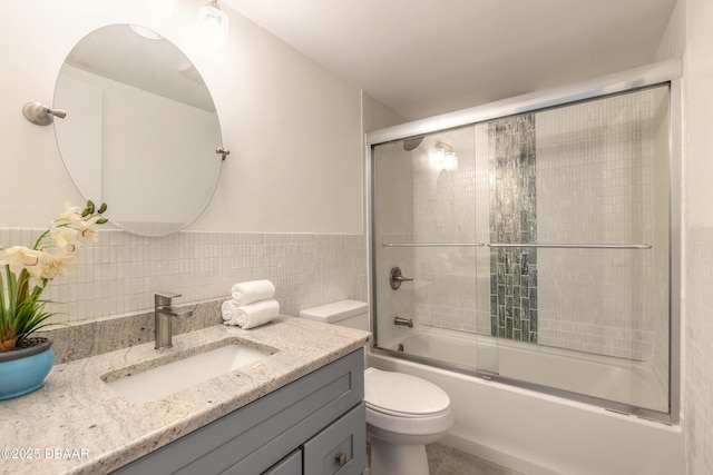 bathroom with tile walls, bath / shower combo with glass door, toilet, wainscoting, and vanity