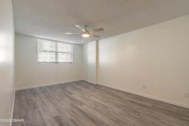 spare room featuring baseboards, wood finished floors, and a ceiling fan