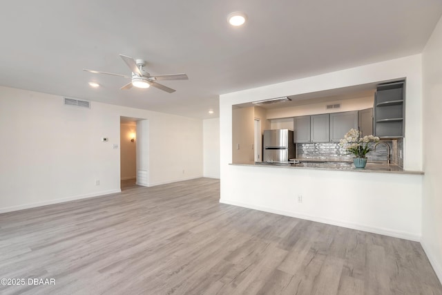 unfurnished living room featuring visible vents, baseboards, light wood-style floors, and ceiling fan