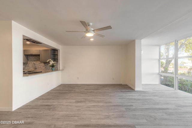 spare room with a sink, a ceiling fan, light wood-type flooring, and baseboards