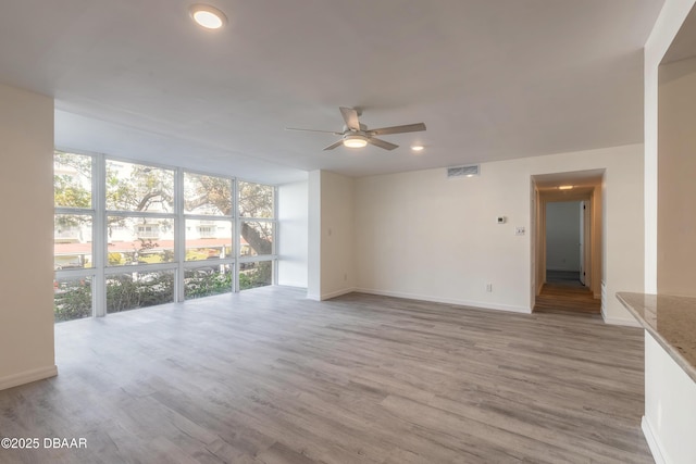 unfurnished living room featuring a wall of windows, a ceiling fan, visible vents, baseboards, and light wood-style flooring