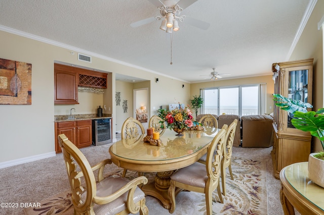 3801 S Atlantic Ave Unit 303, Daytona Beach Shores, FL 32118 - dining space featuring bar with sink, wine cooler, ornamental molding, light carpet, and ceiling fan