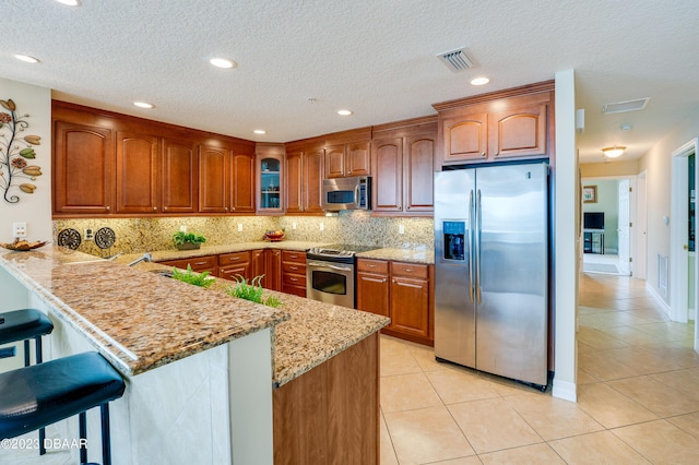 3801 S Atlantic Ave Unit 303, Daytona Beach Shores, FL 32118 - kitchen featuring stainless steel appliances, a peninsula, light tile patterned floors, light stone countertops, and a breakfast bar