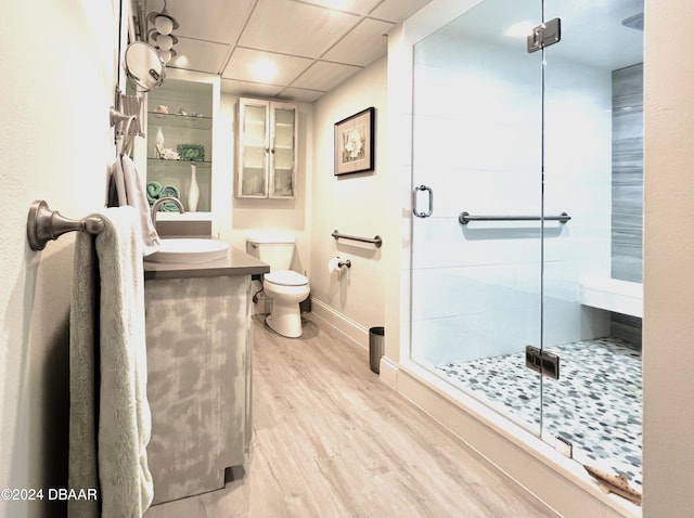 bathroom with wood-type flooring, vanity, toilet, a drop ceiling, and a shower with shower door