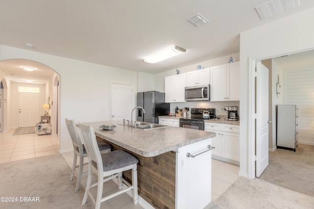 kitchen featuring stainless steel appliances, light colored carpet, a center island with sink, sink, and white cabinetry