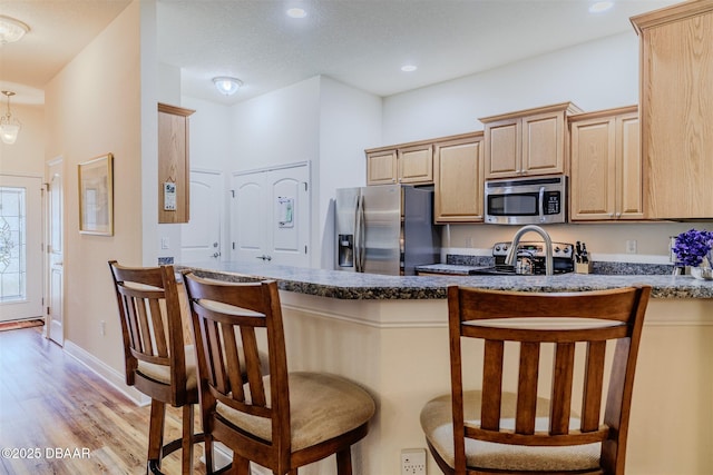 kitchen with a breakfast bar, dark stone countertops, light wood-type flooring, light brown cabinets, and stainless steel appliances