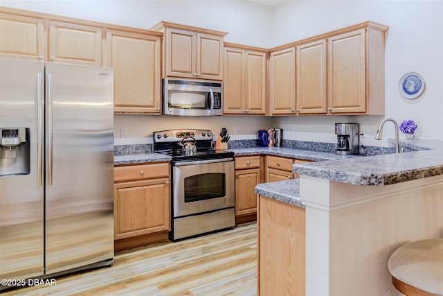 kitchen with light brown cabinetry, stainless steel appliances, light hardwood / wood-style floors, and kitchen peninsula