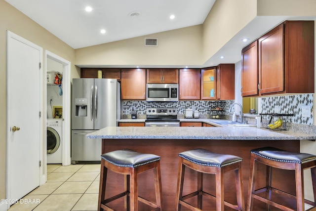 kitchen with a kitchen breakfast bar, stainless steel appliances, washer / clothes dryer, light tile patterned flooring, and sink