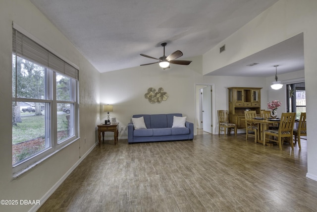 living area with visible vents, ceiling fan, baseboards, vaulted ceiling, and wood finished floors