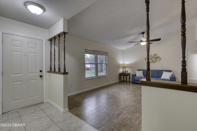 entrance foyer with baseboards, a textured ceiling, a ceiling fan, and vaulted ceiling