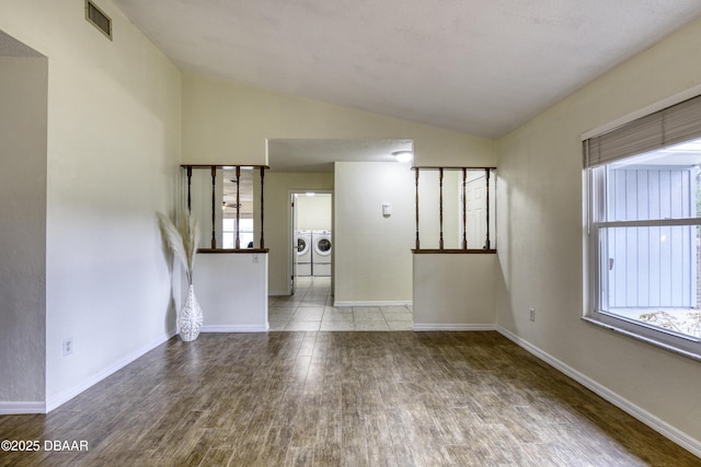 empty room with visible vents, baseboards, washer and clothes dryer, lofted ceiling, and wood finished floors