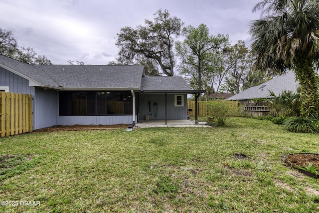 back of property with a shingled roof, a sunroom, a fenced backyard, a yard, and a patio area