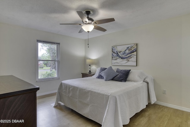 bedroom featuring ceiling fan, baseboards, a textured ceiling, and wood finished floors