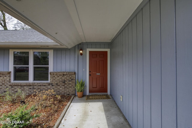 doorway to property featuring brick siding and a shingled roof