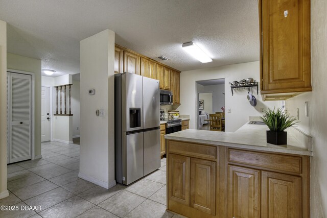 kitchen featuring a peninsula, light tile patterned flooring, light countertops, appliances with stainless steel finishes, and a textured ceiling