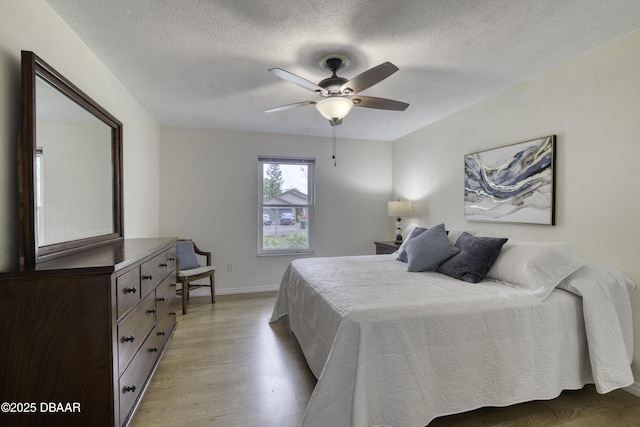 bedroom with light wood-type flooring, baseboards, a textured ceiling, and ceiling fan