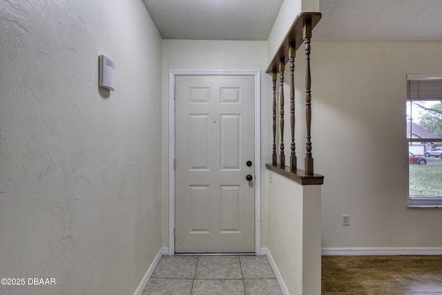 doorway featuring light tile patterned floors, a textured ceiling, baseboards, and a textured wall