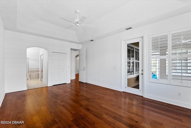 interior space with ceiling fan, a tray ceiling, and dark hardwood / wood-style flooring