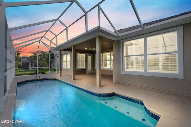 pool at dusk featuring a patio area, a lanai, and ceiling fan