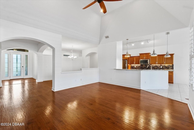 unfurnished living room featuring sink, light wood-type flooring, ceiling fan with notable chandelier, and high vaulted ceiling