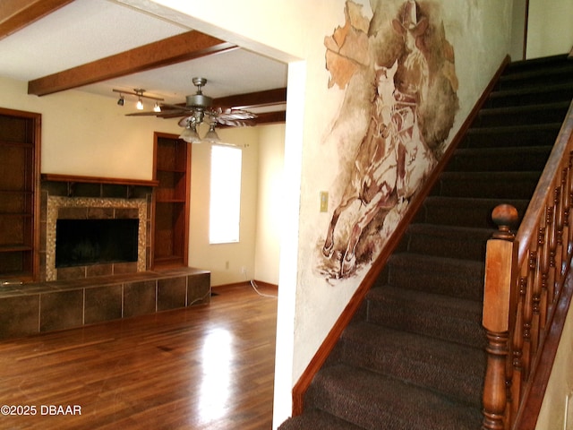 stairs featuring beam ceiling, a fireplace, ceiling fan, and hardwood / wood-style flooring