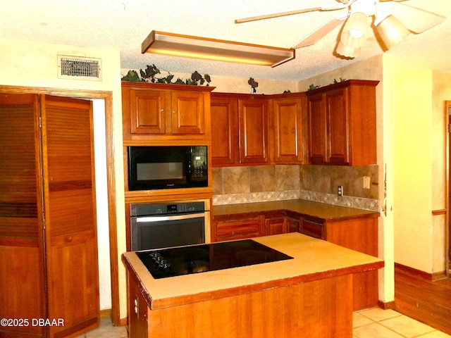 kitchen featuring light tile patterned flooring, black appliances, a kitchen island, ceiling fan, and backsplash