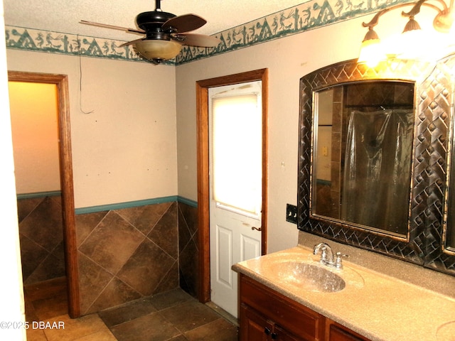 bathroom with ceiling fan, tile walls, vanity, a textured ceiling, and walk in shower