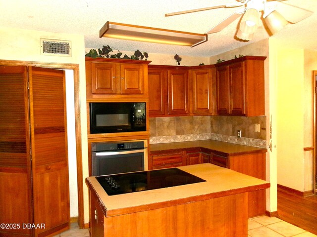 kitchen featuring light tile patterned floors, ceiling fan, black appliances, a kitchen island, and decorative backsplash