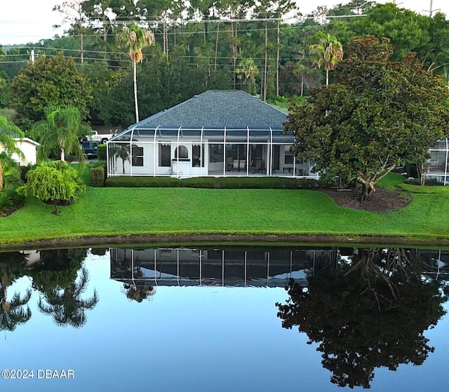 back of property with a water view, glass enclosure, and a lawn