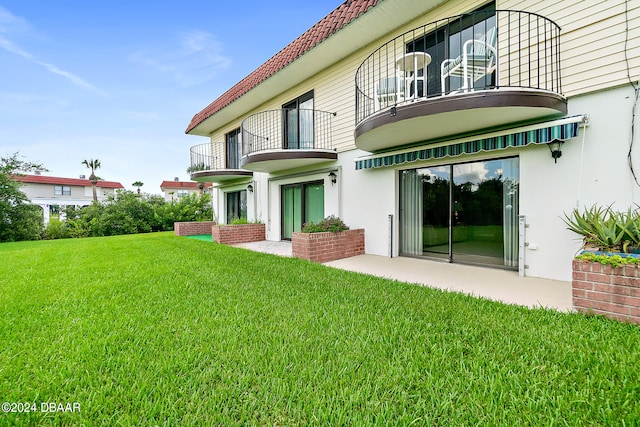 rear view of house with a patio, a balcony, and a yard