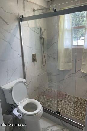 bathroom featuring toilet, tile walls, and a shower with door