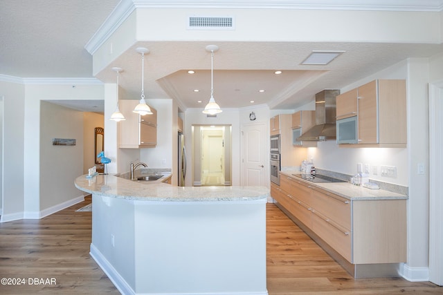 kitchen featuring light brown cabinetry, kitchen peninsula, decorative light fixtures, and wall chimney exhaust hood