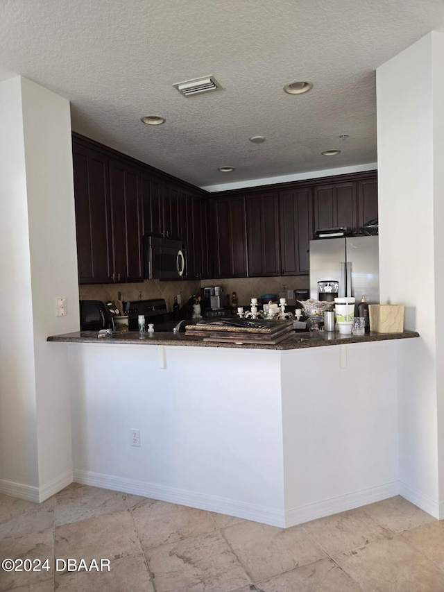 kitchen featuring dark stone counters, kitchen peninsula, a textured ceiling, dark brown cabinets, and appliances with stainless steel finishes