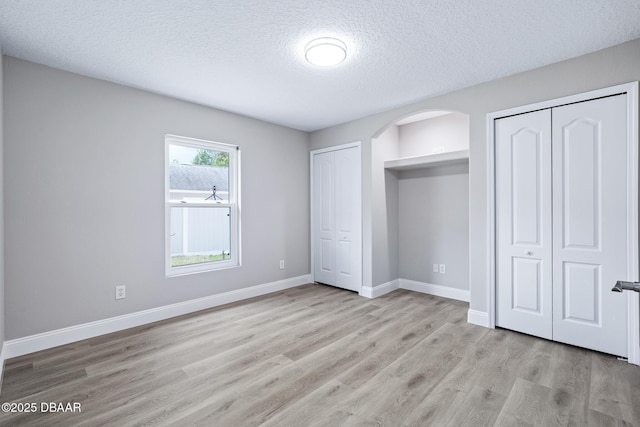 7 Traceway Ct, Ormond Beach, FL 32174 - unfurnished bedroom with two closets, light wood-style flooring, a textured ceiling, and arched walkways