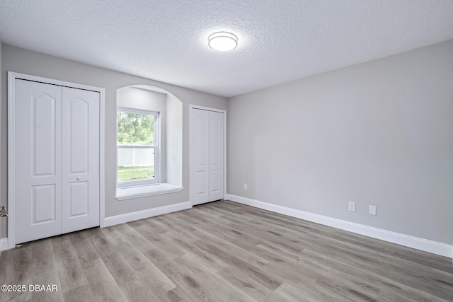 7 Traceway Ct, Ormond Beach, FL 32174 - unfurnished bedroom featuring multiple closets, a textured ceiling, arched walkways, and wood finished floors