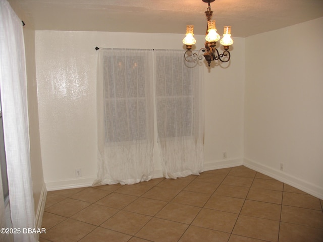 tiled empty room with baseboards and a chandelier