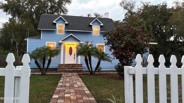 view of front of property with a fenced front yard, roof with shingles, a chimney, entry steps, and a front lawn