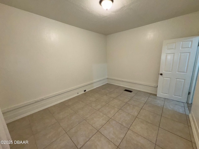 unfurnished room with light tile patterned floors, baseboards, visible vents, and a textured ceiling