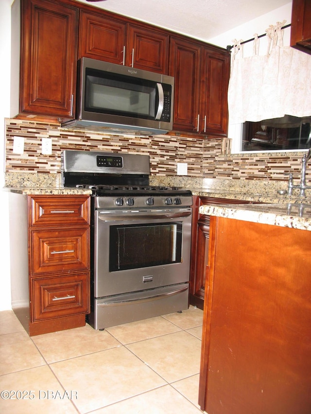 kitchen featuring stainless steel appliances, backsplash, light stone counters, and light tile patterned floors